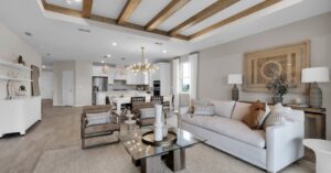 Pulte Homes Wildlight open concept living room, dining room and kitchen with white cabinets and counter tops and five wood beams on the ceiling.