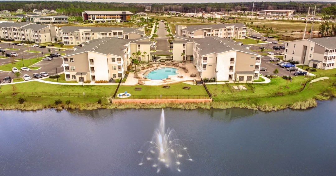 Wildlight, FL - The Lofts at Wildlight apartment complex sits on edge of lake with water fountain. Overhead shot of buildings, pool and lake.