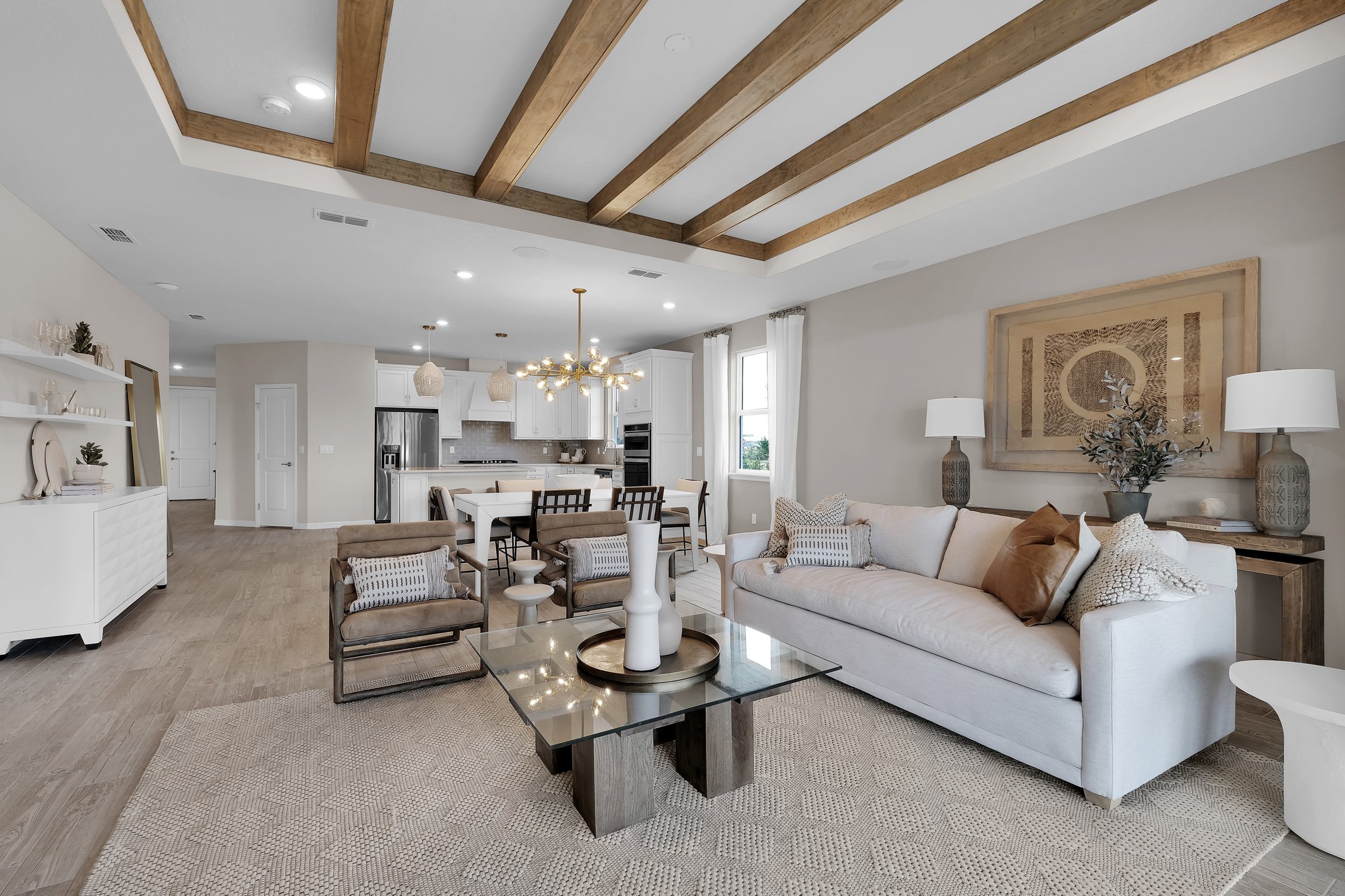 Pulte Homes Wildlight open concept living room and kitchen with five wood beams on the ceiling. Furniture is white and cream.