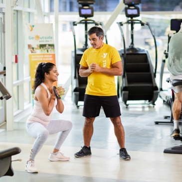 A man and woman in a gym doing squats.