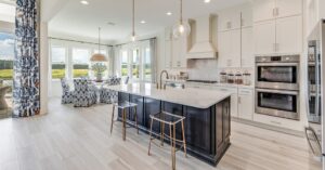 Del Webb Wildlight home interior. Open concept kitchen, living, dining. White cabinets and countertops. Large island with dark cabinets and white countertops. Light wood floors.