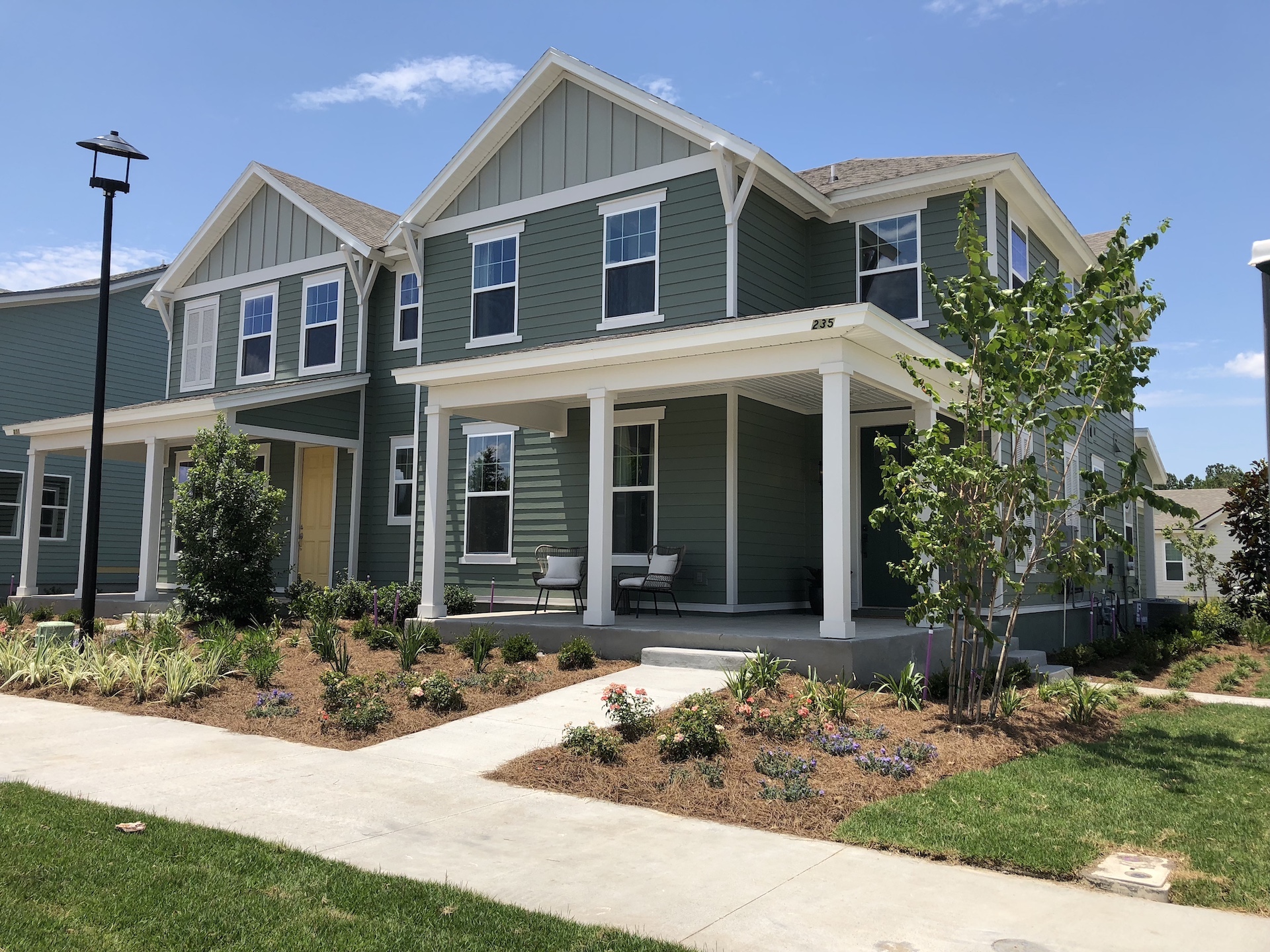 Dostie Homes Wildlight two-story townhomes with green exterior and white trim and large front porch.