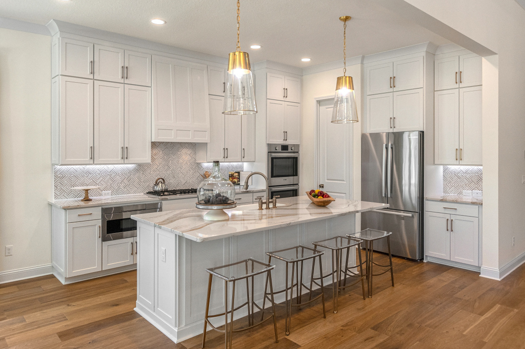 Riverside Homes open kitchen with floor to ceiling white cabinets, large island with marble counters and two pendant lights.