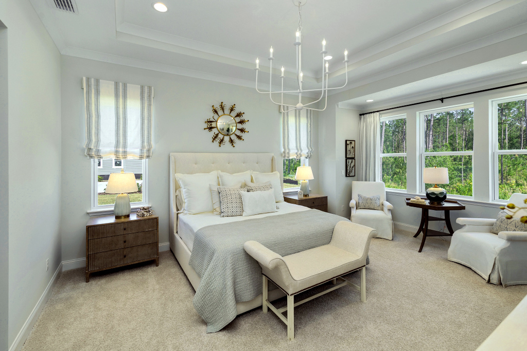 Riverside Homes Wildlight owner's suite with five large windows, chandelier, king size bed and seating area.