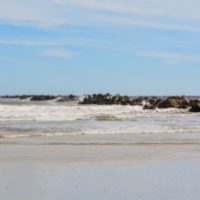 Beach with waves coming in and a line of black rocks in the distance at Little Talbot Island.