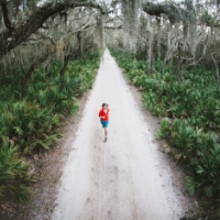 Birds eye view of a person in a red jacket standing on a gravel trail at Cumberland Island National Seashore, with trees and woods surrounding them.