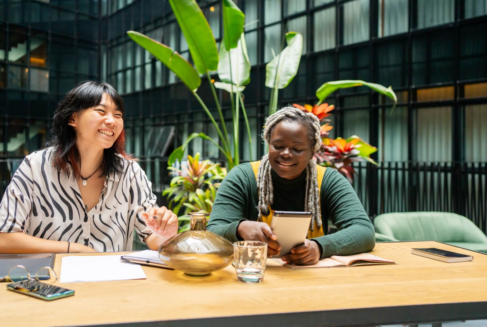 Asian and Black female colleagues having fun and sitting at a table in an open co-working space.