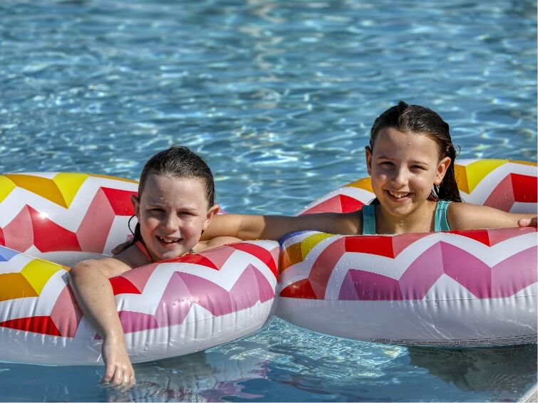 Two young girls floating in a pool on red, pink and white pool tubes at Waterbug Park in Wildlight.