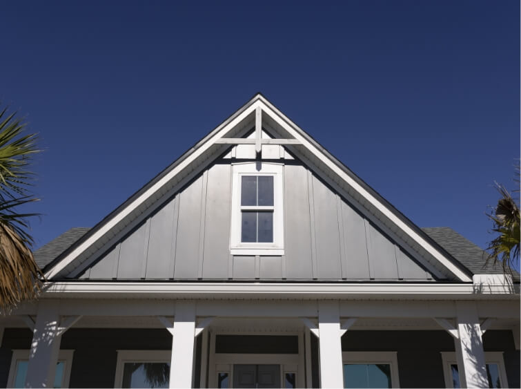 Roofline of a grey house with white accents. The top of the house has one window with four columns beneath.