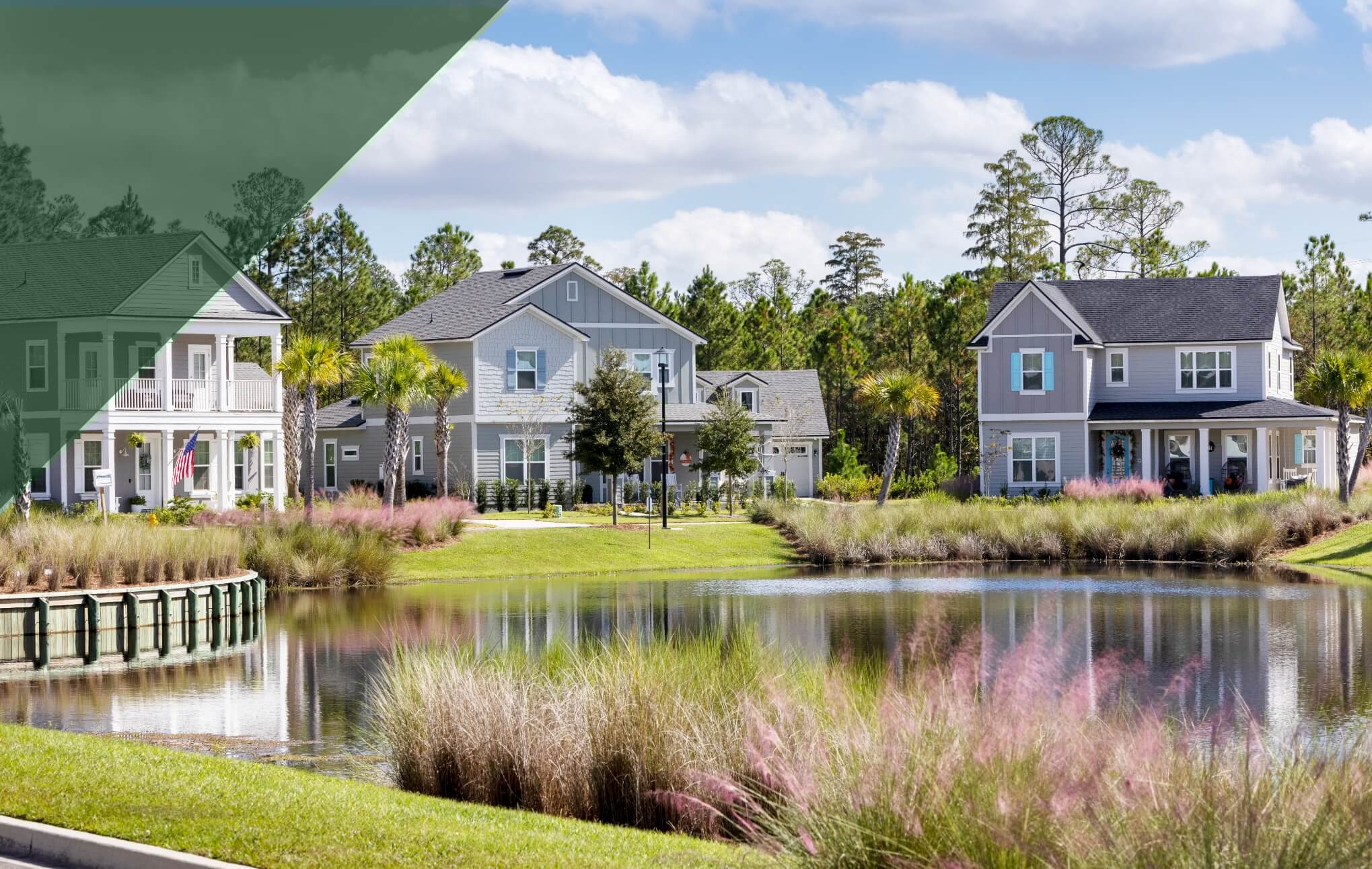 A small pond with three, two story homes across the water and trees behind the houses.