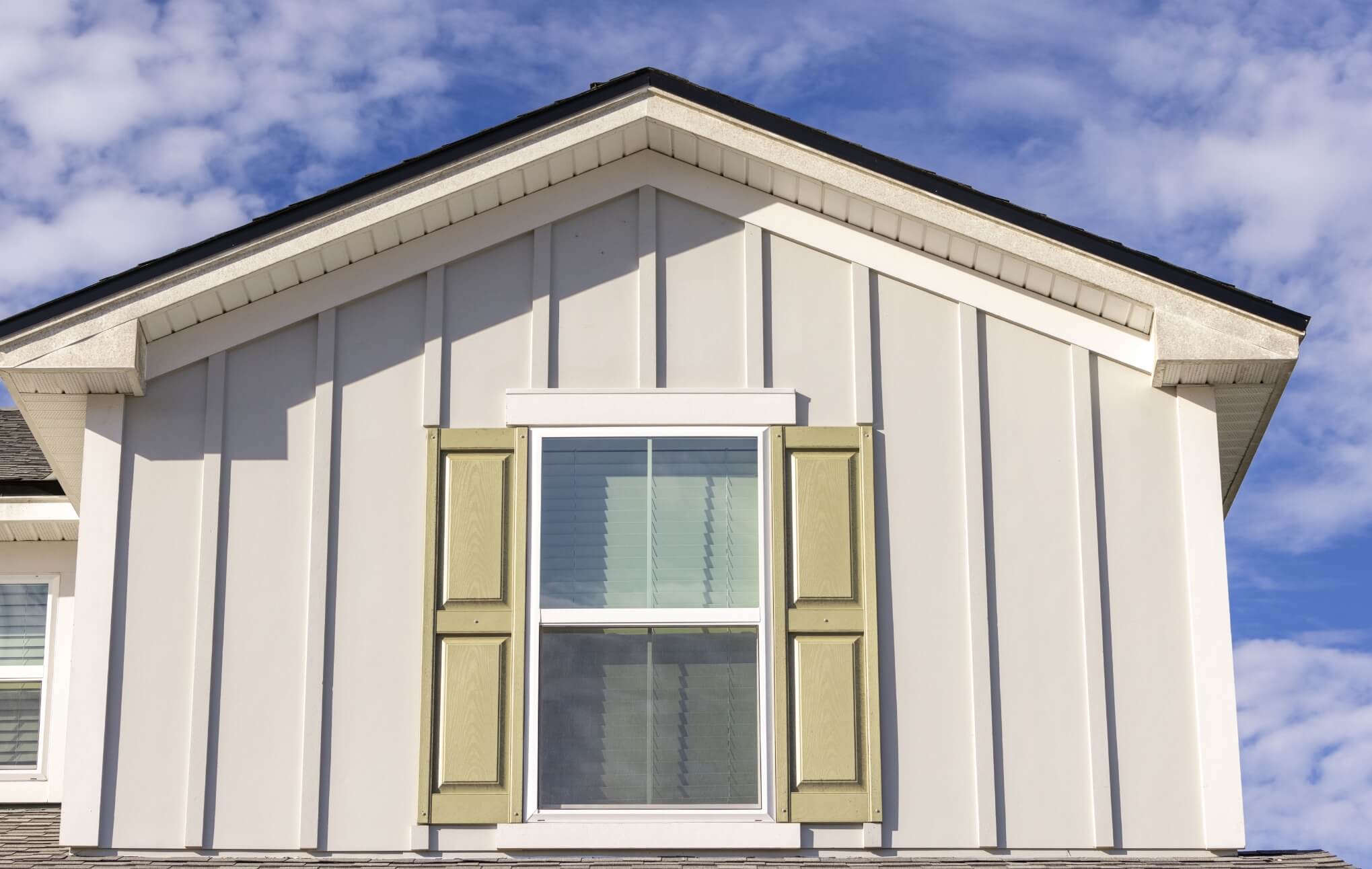 Close up of a pointed roofline and window with light green shutters.