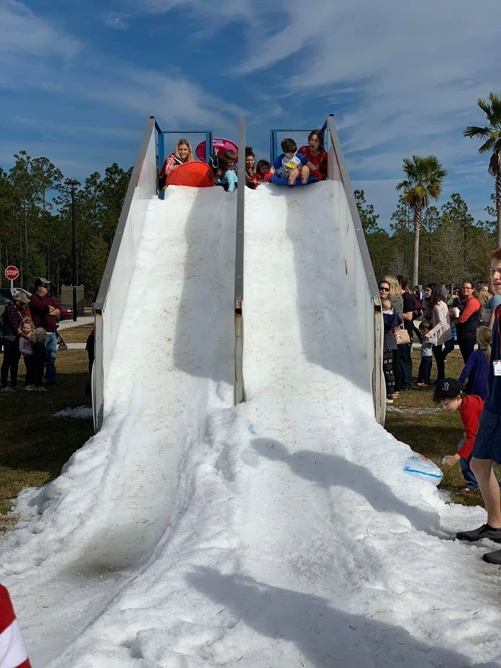 Two children go down a slide made of snow at a community event at Wildlight.