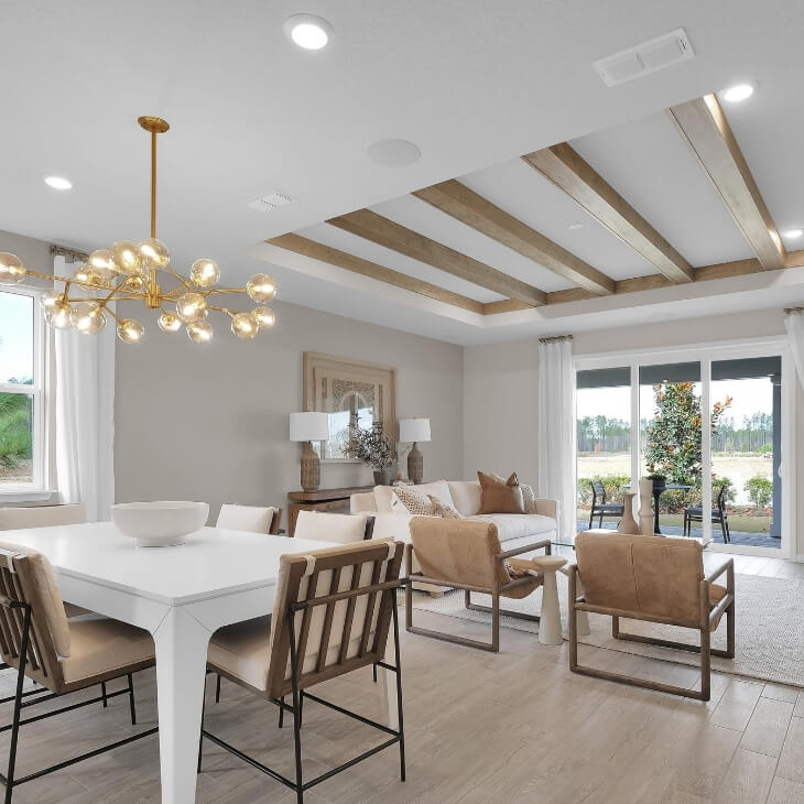 White dining room and living room with coved ceiling that feature wood beam accents. The room has sliding doors that lead to a back patio.