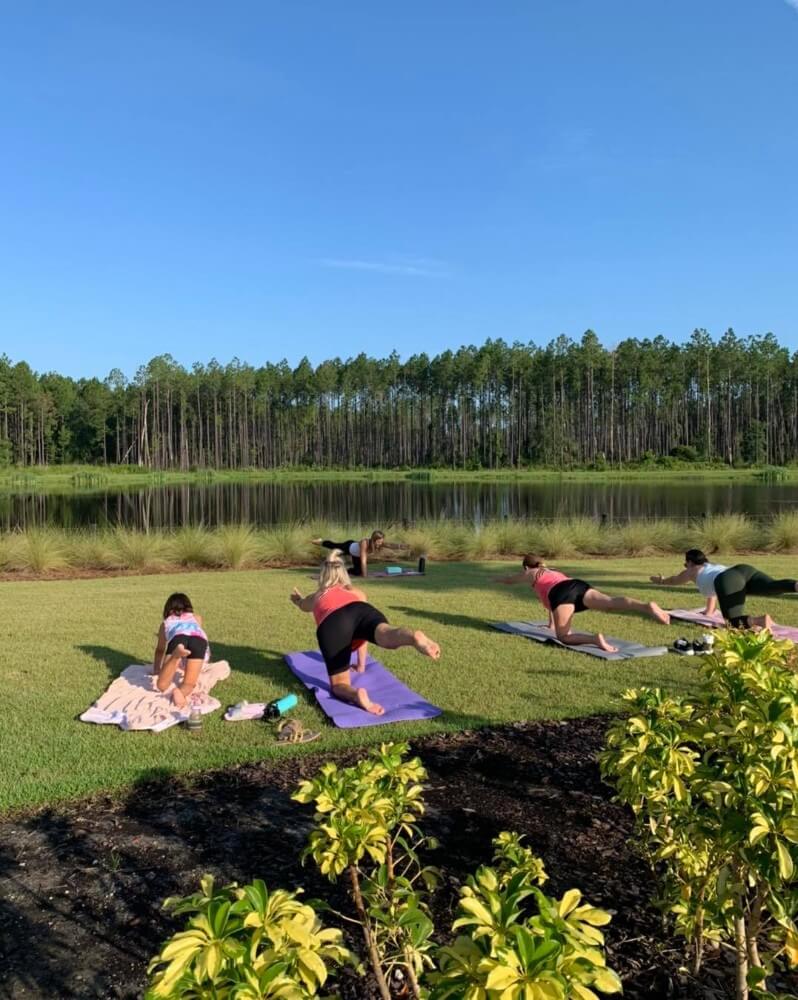 A group of people doing yoga in the grass near a lake.