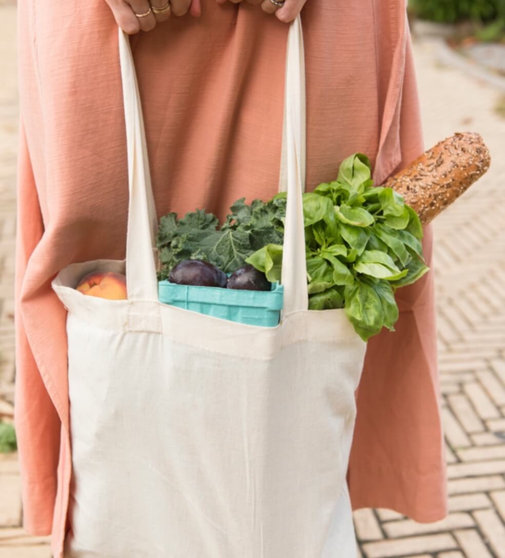 A woman holding a tote bag full of vegetables.