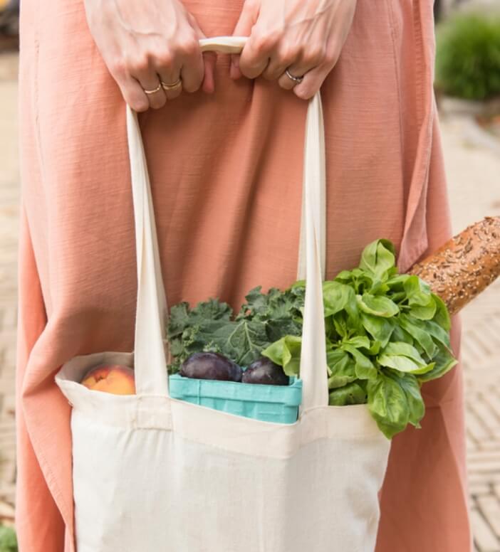 A woman holding a tote bag full of vegetables.