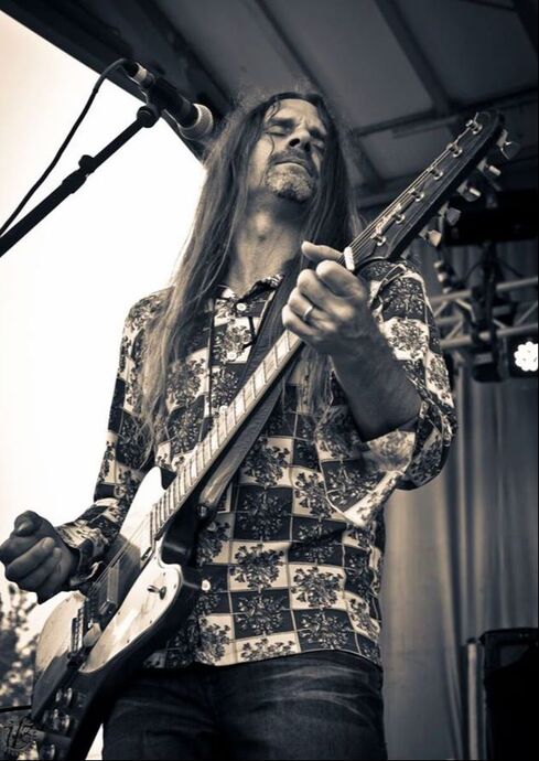 A man with long hair playing a guitar in front of a microphone.