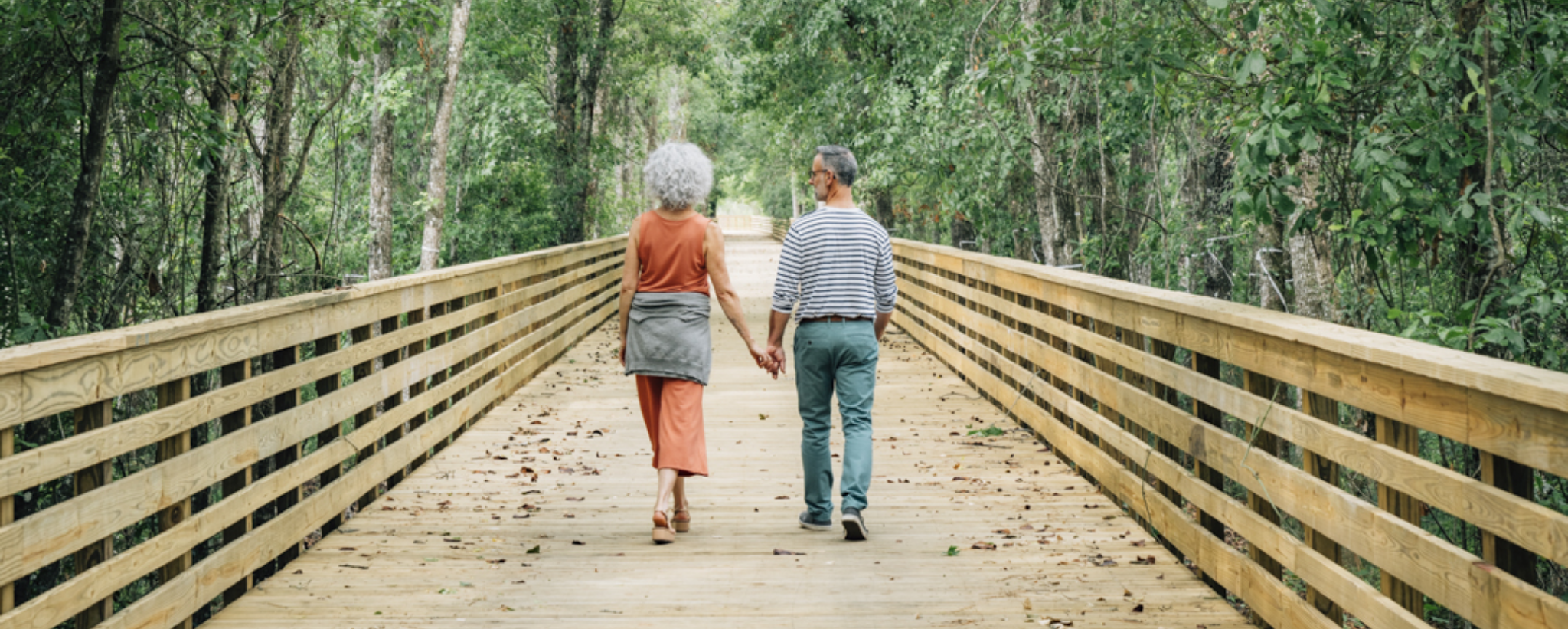 A couple walking on a wooden bridge in the woods.