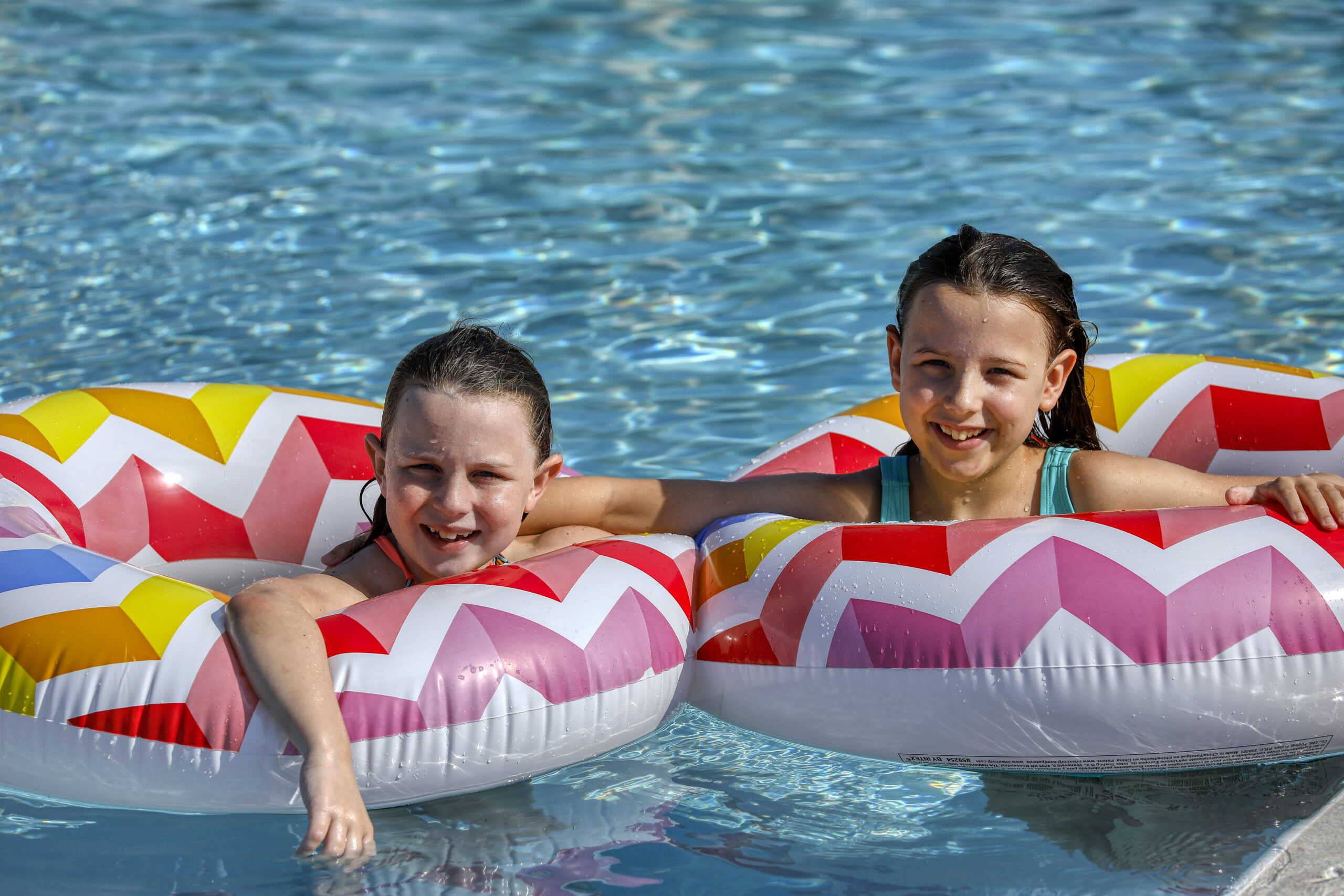 Two young girls are floating in a pool with inflatable tubes.