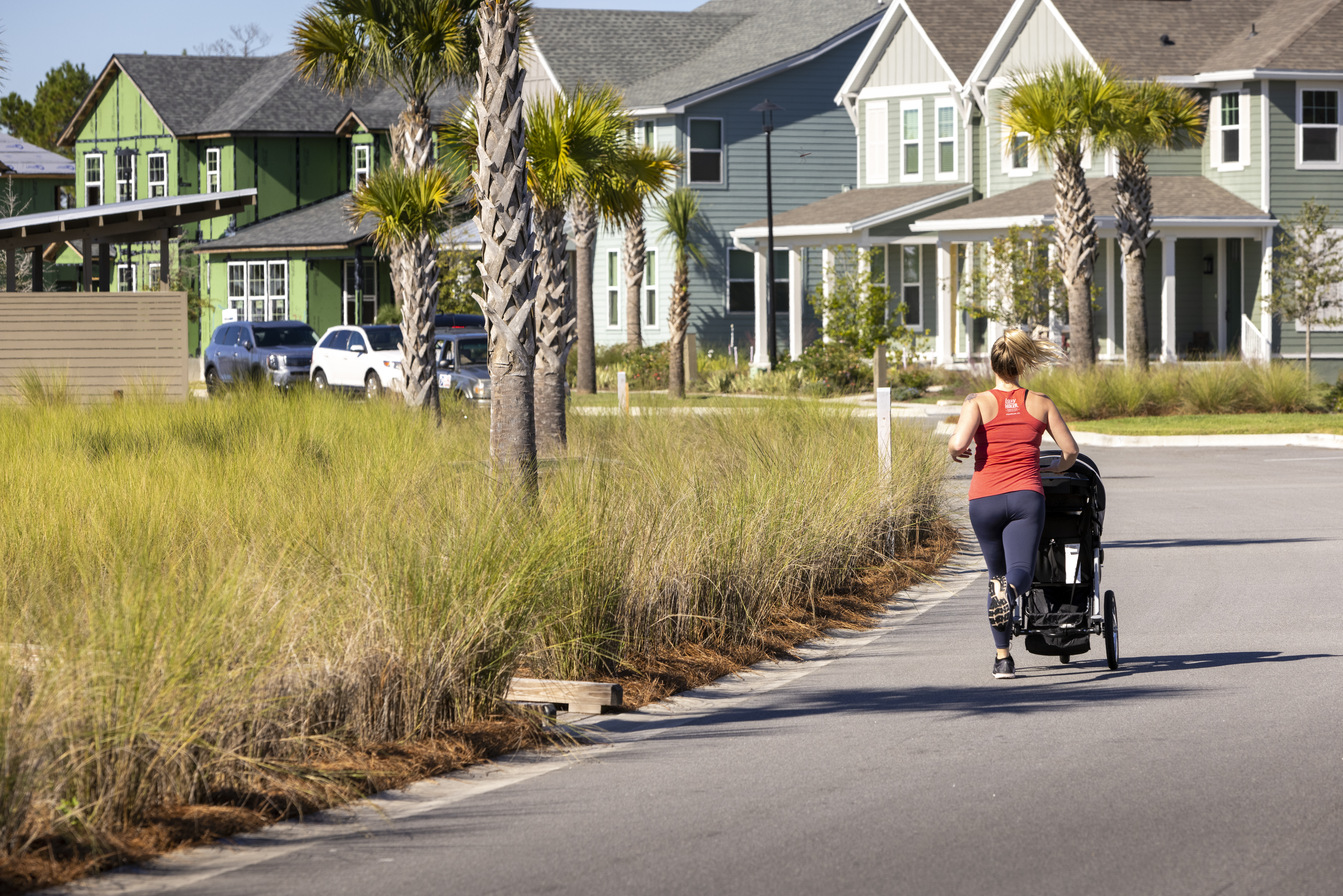 Woman with stroller going for a jog in neighborhood with palm trees.