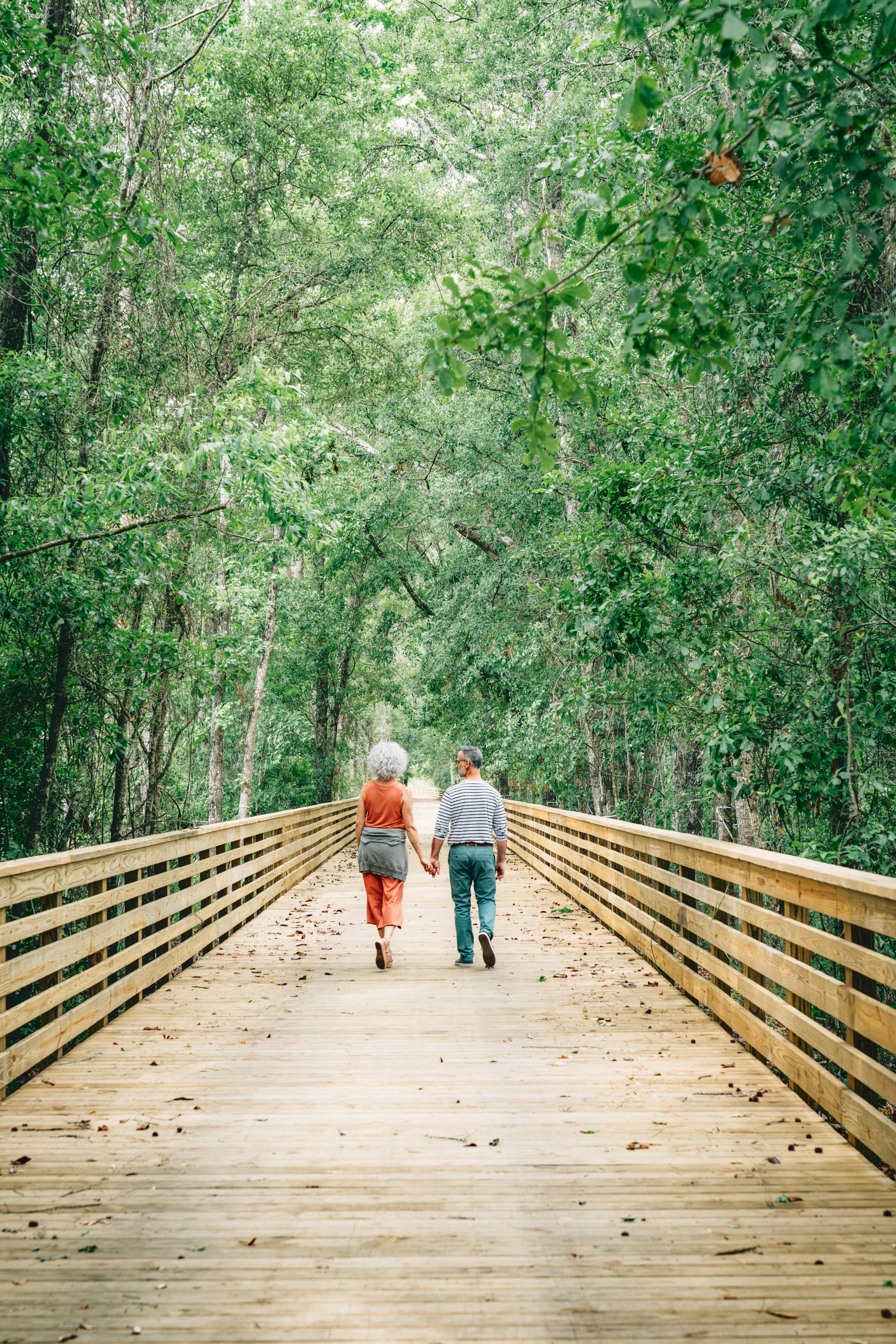 A middle-aged couple holds hands while walking down a boardwalk.