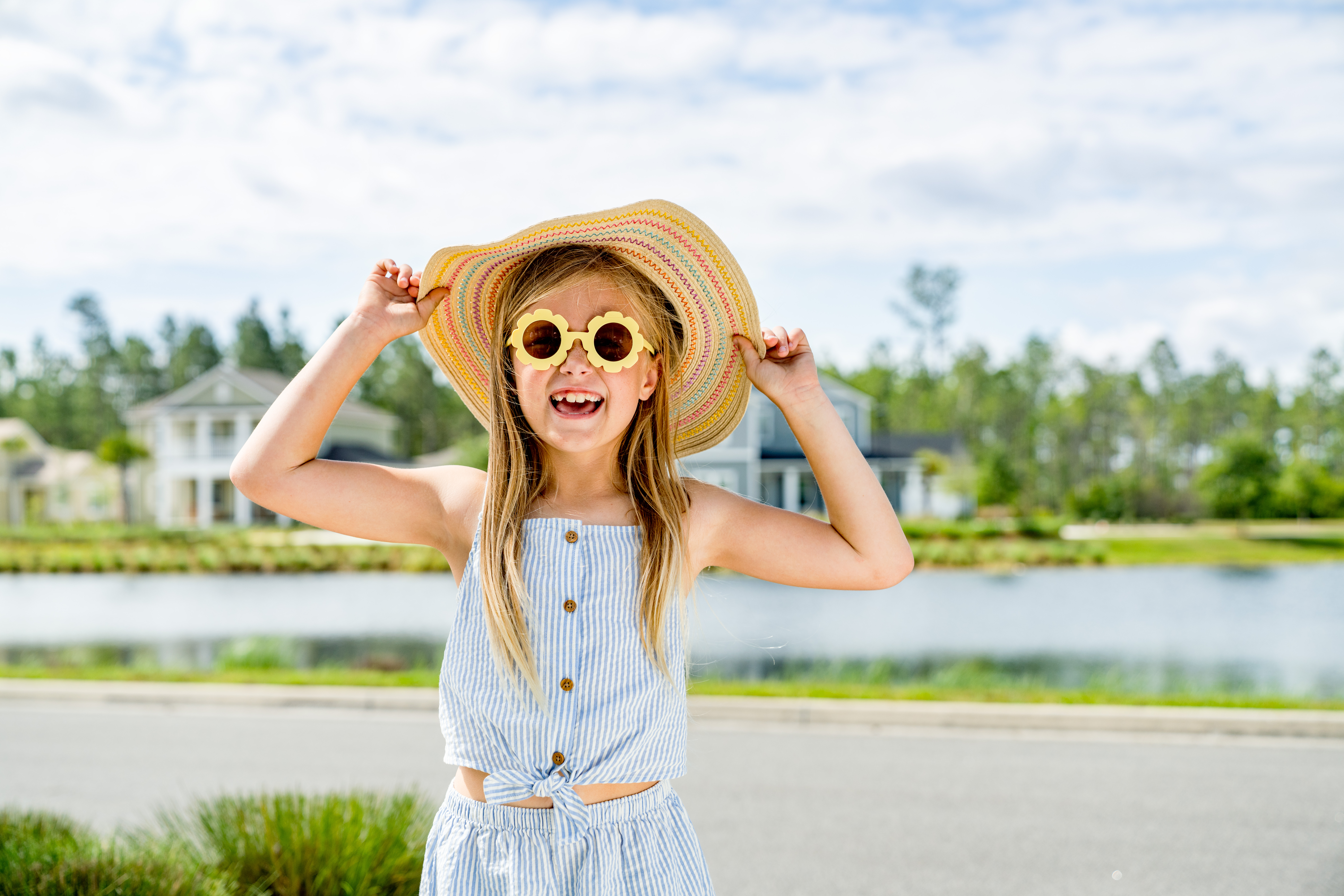 Young girl wearing a sunhat and flower sunglasses plays outside.