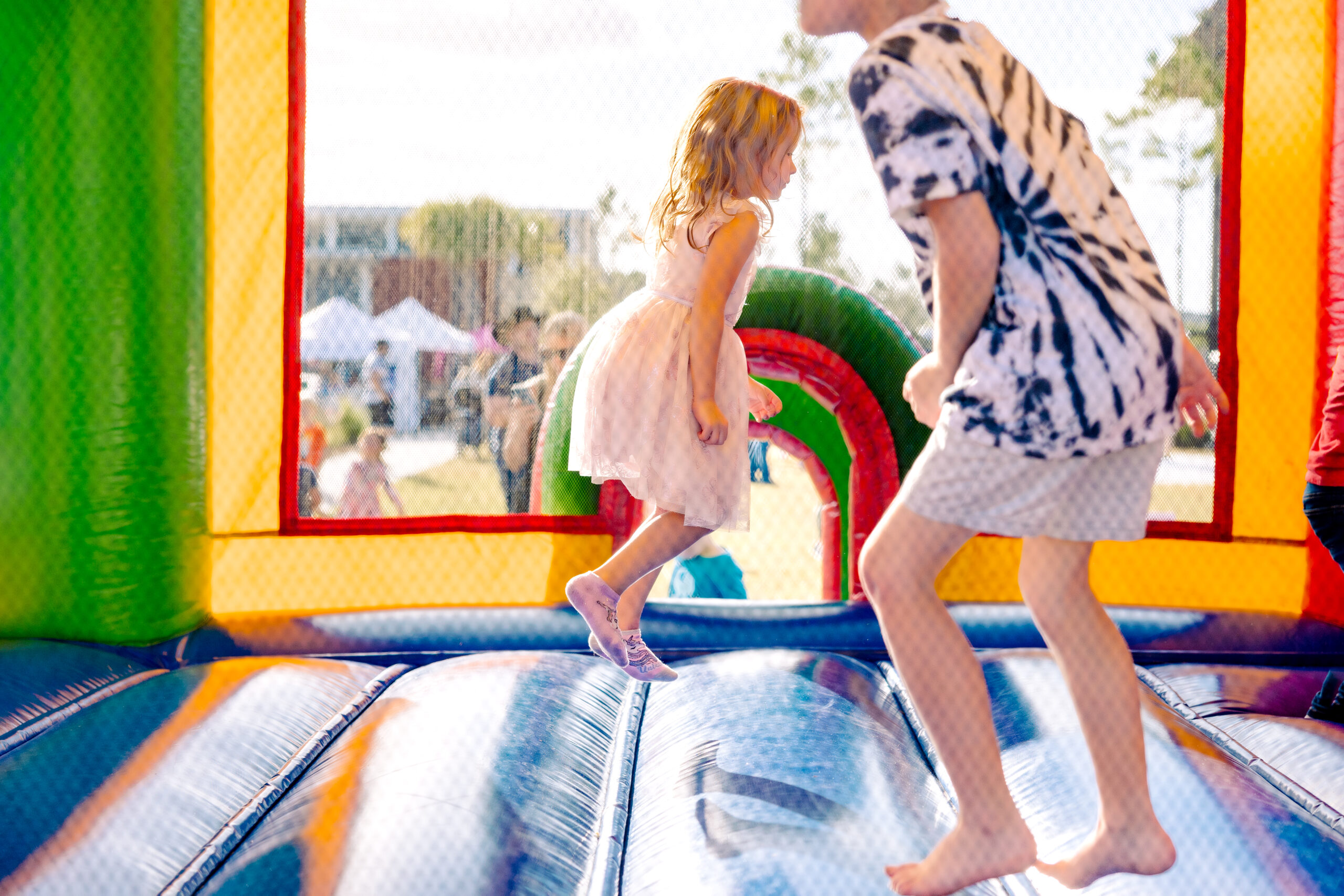 Two children playing on an inflatable bouncer at an outdoor event.