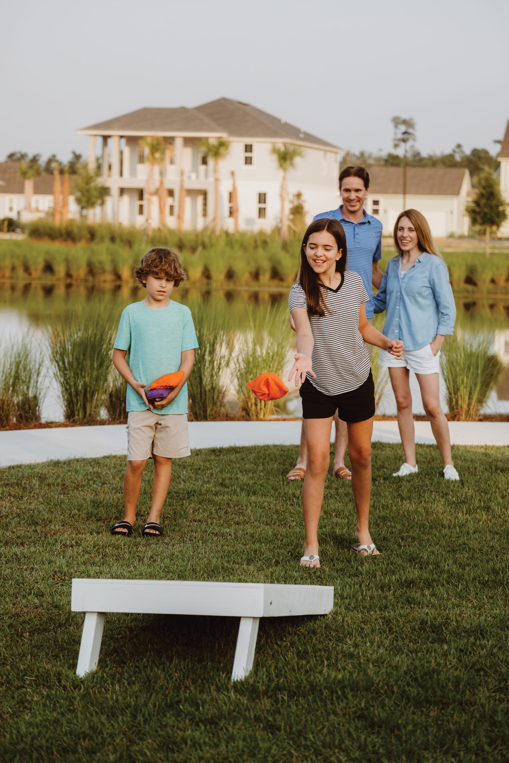 A family playing cornhole on a lawn near a pond.