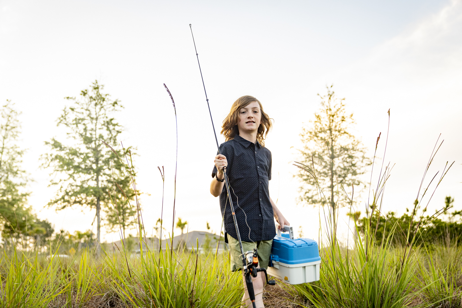 A young boy holding a fishing pole in the grass.