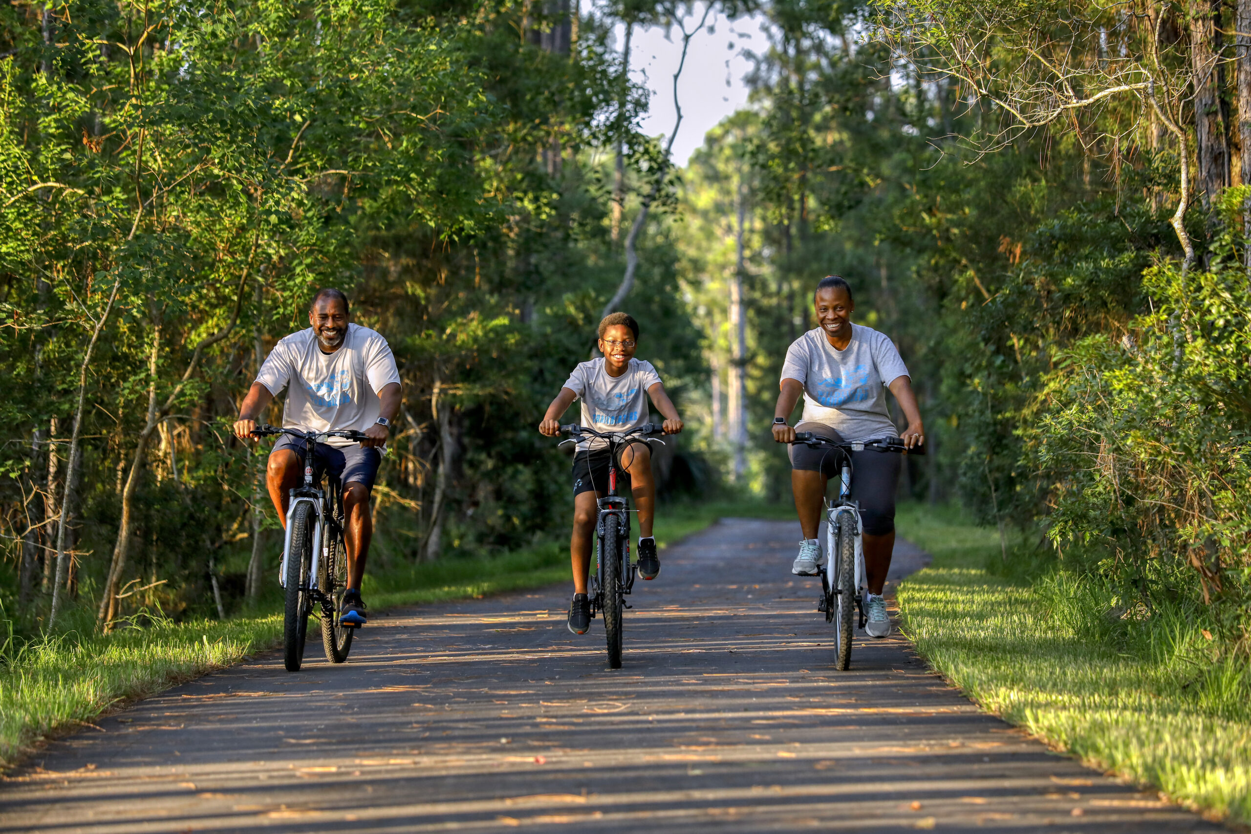 Three people riding bicycles down a path in a wooded area.