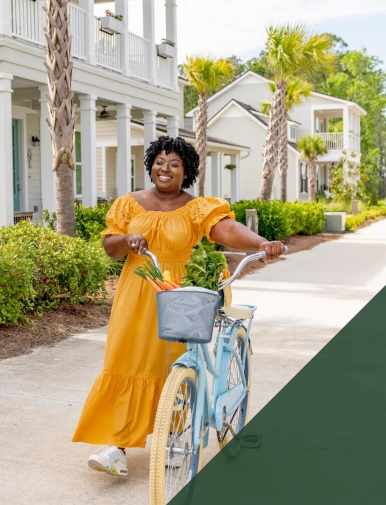 A woman in a yellow dress with a bicycle in front of a house.