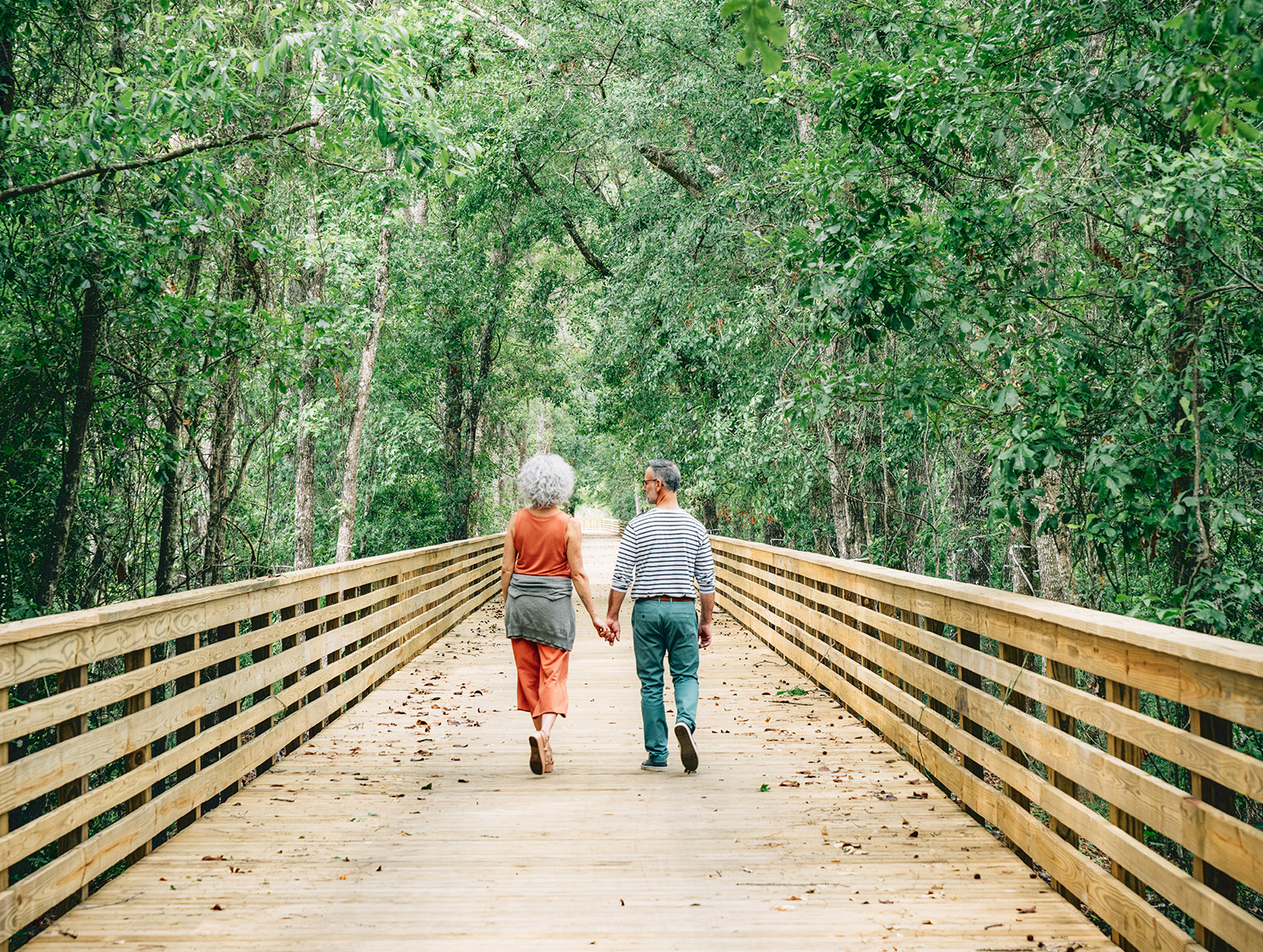 A couple holds hands while walking down a boardwalk.