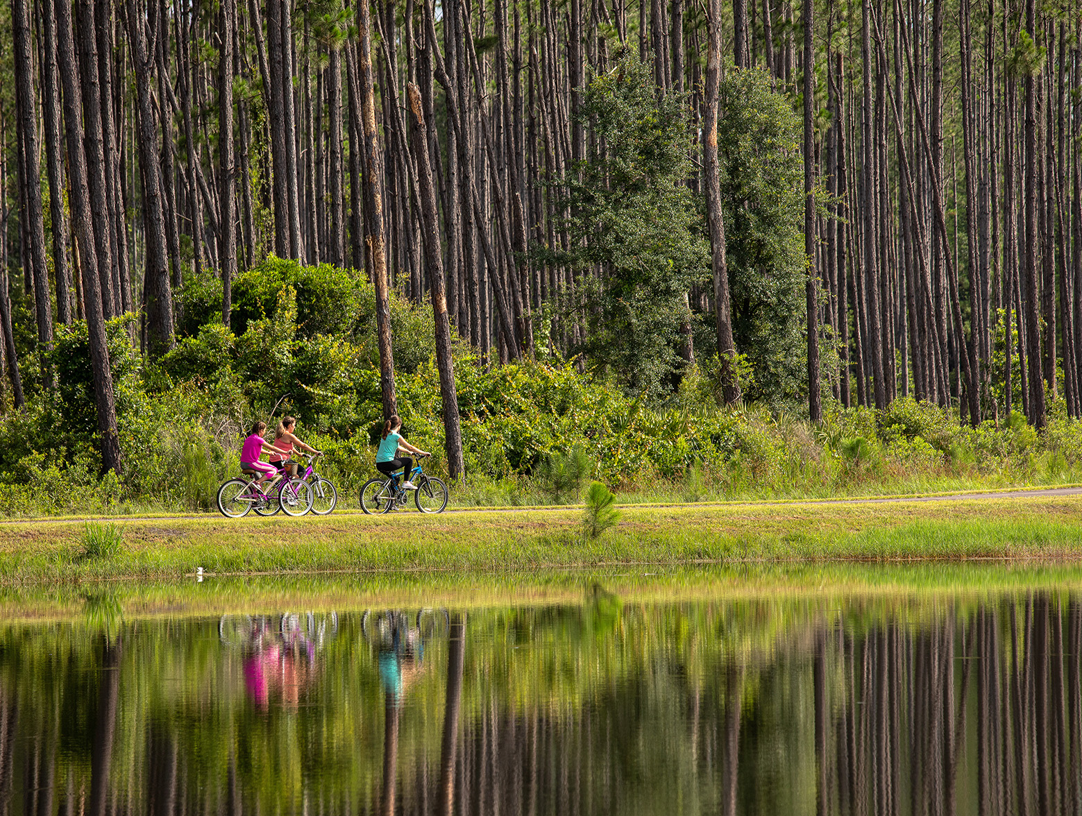 Three people ride bikes down path with reflection in the water.