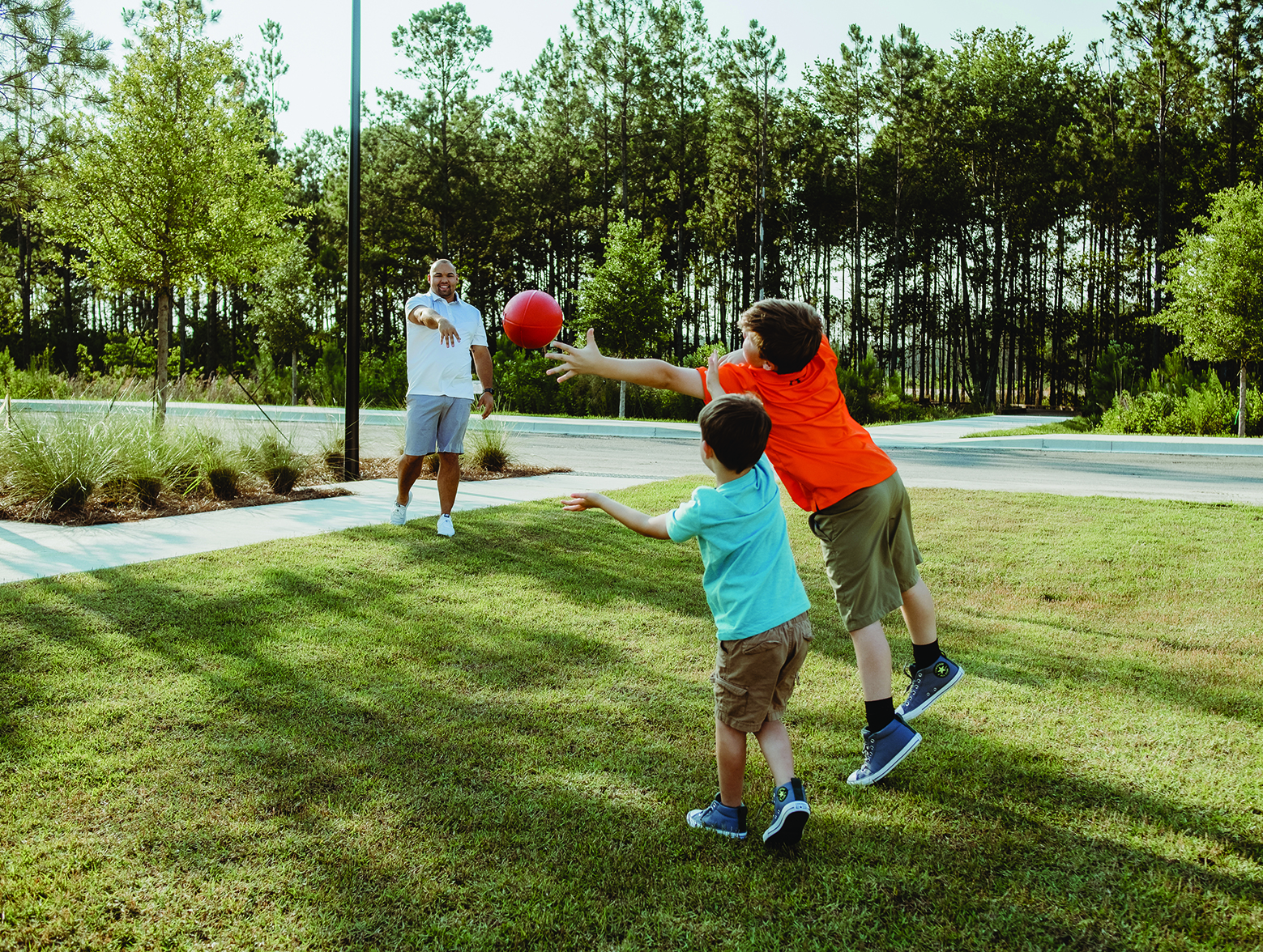 Dad tosses football with two boys in yard.