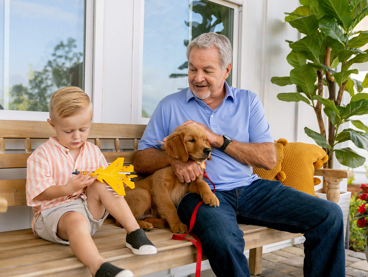 Grandpa, toddler and puppy sit on bench.