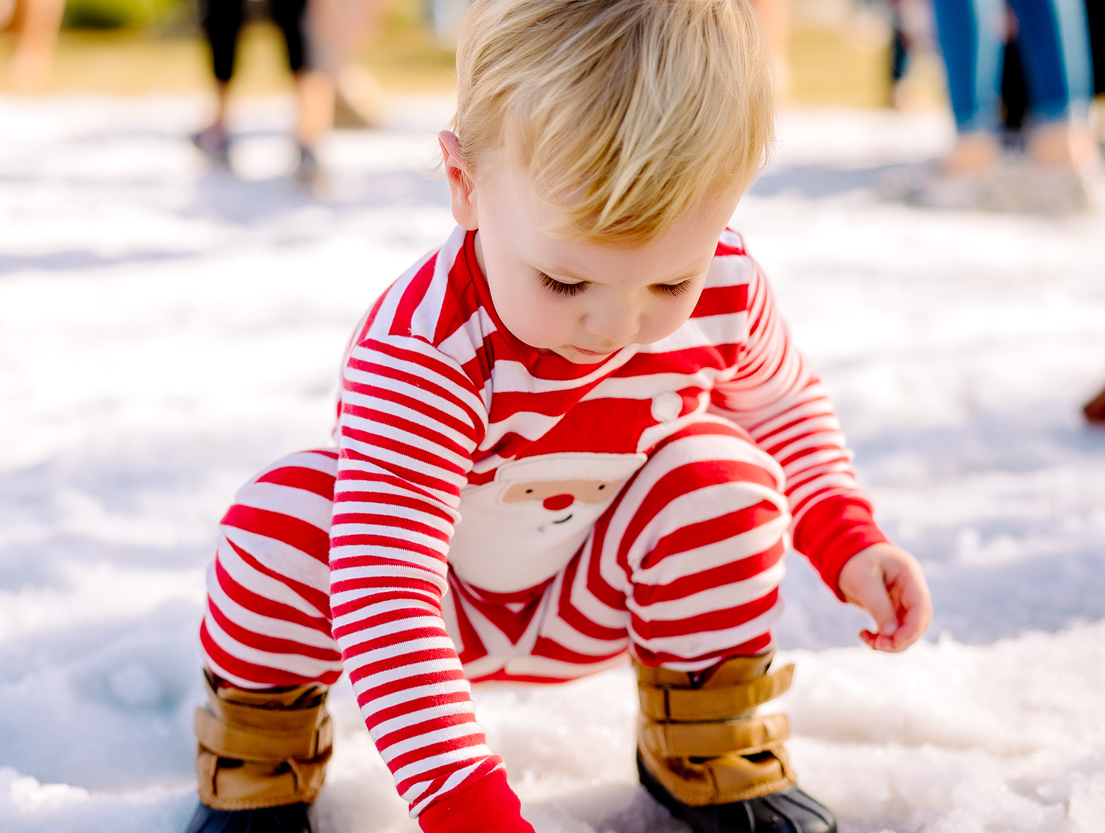 Child in Christmas pajamas and boots plays in snow at Winterfest.