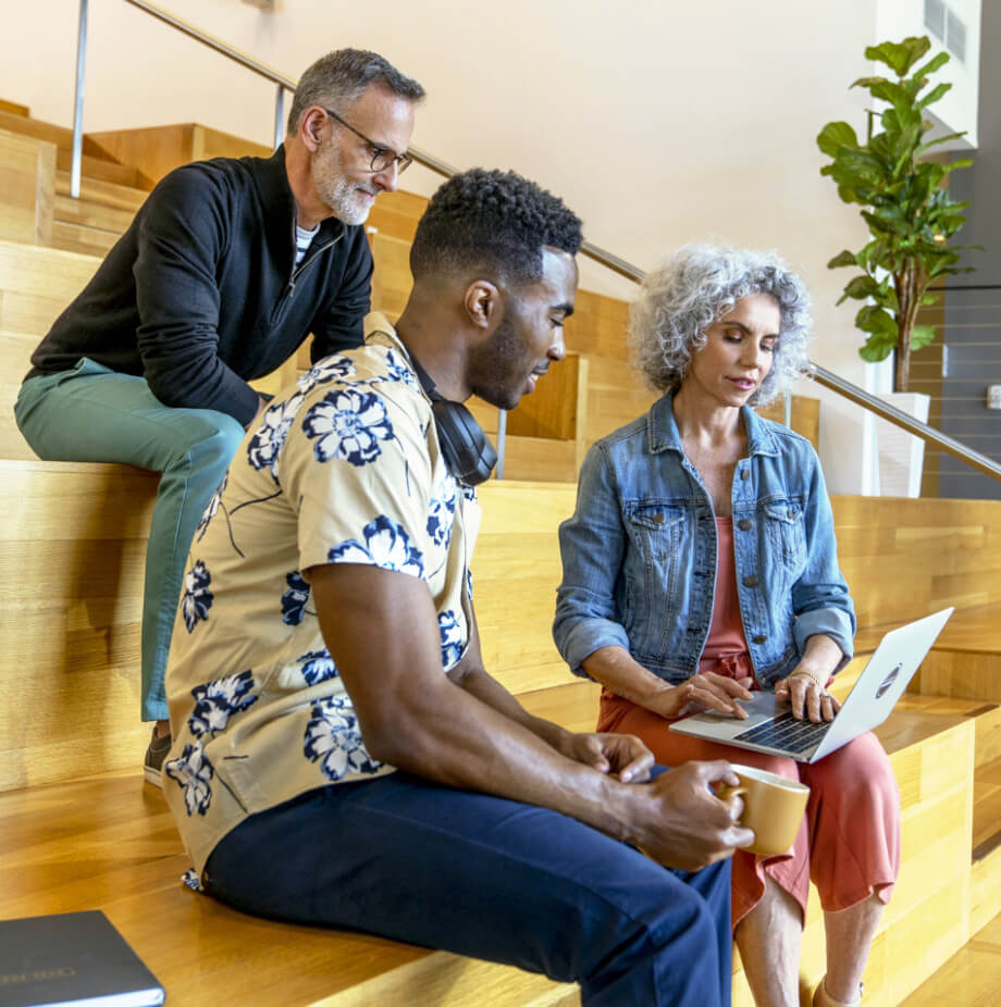 A group of people sitting on stairs and looking at a laptop.