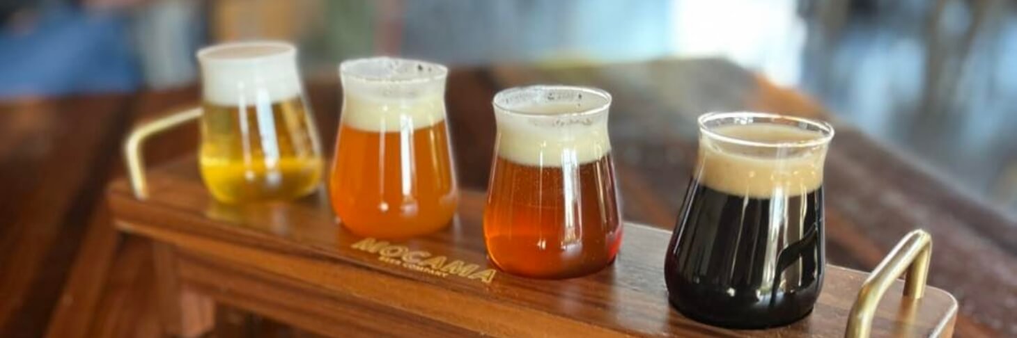 Four different beers are sitting on a wooden tray.