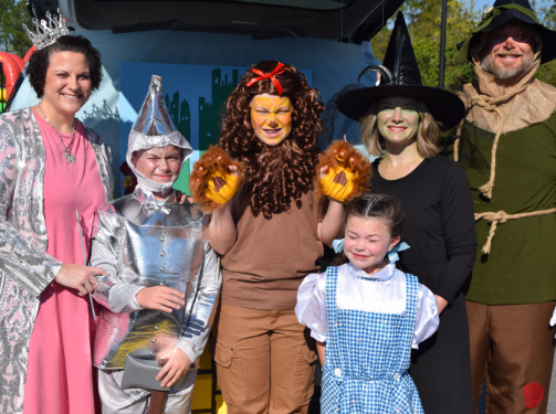 Six people in Wizard of Oz costumes stand and smile outdoors in the Wildlight Yulee Florida community, dressed as Glinda, Tin Man, Cowardly Lion, Dorothy, Wicked Witch, and Scarecrow.