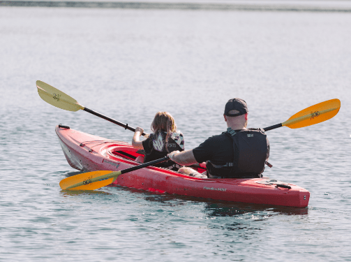 Two people wearing life jackets paddle a red kayak together on calm water, facing away from the camera, enjoying an outdoor adventure near the Wildlight Florida community and the scenic homes in Nassau County, Florida.