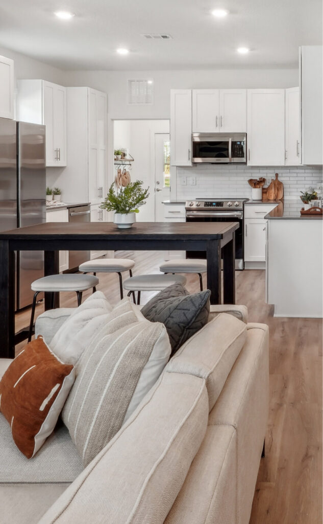 Modern kitchen with white cabinets, stainless steel appliances, a black island with stools, and a beige sofa in the foreground—perfect for enjoying life in the welcoming Wildlight Yulee Florida community.