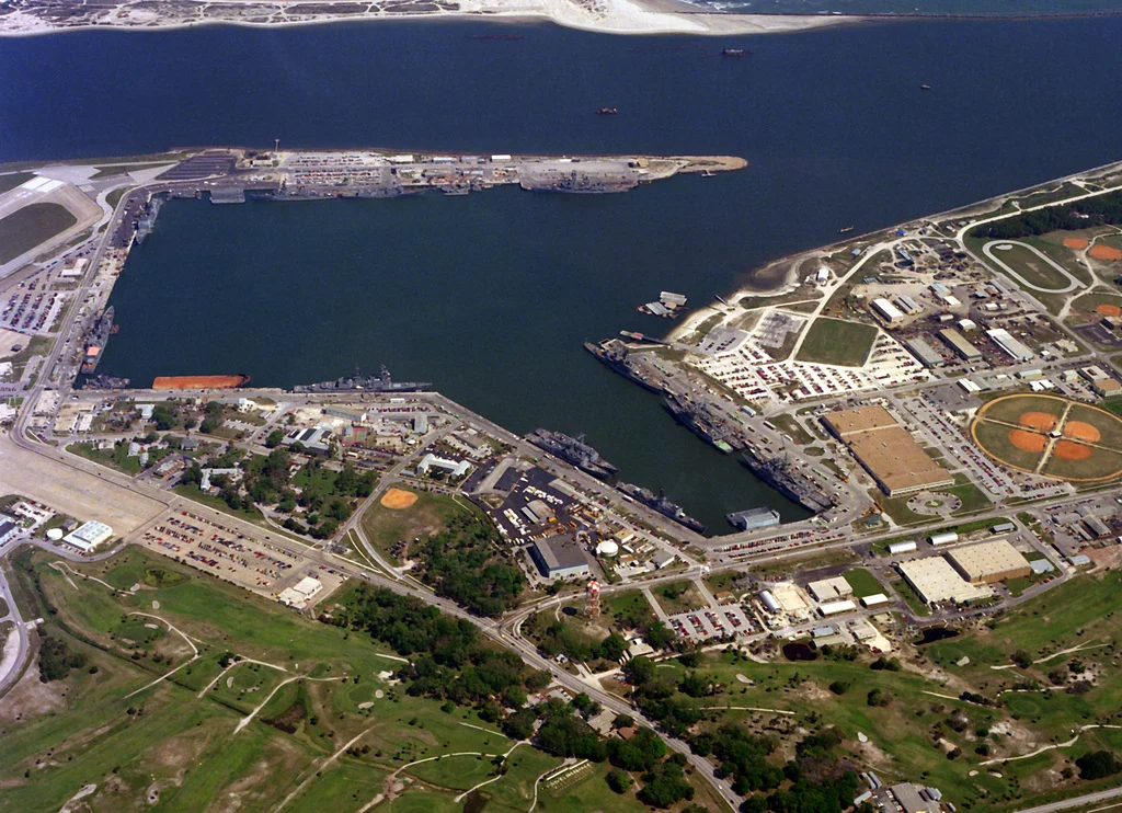 Aerial view of a coastal naval base with docks, ships, buildings, roads, sports fields, and green spaces by the water near the Wildlight Yulee Florida community.