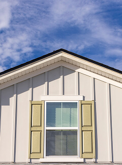The upper portion of a house in the Wildlight Yulee Florida community features vertical siding, a centered window with light green shutters, and a blue sky with scattered clouds overhead.