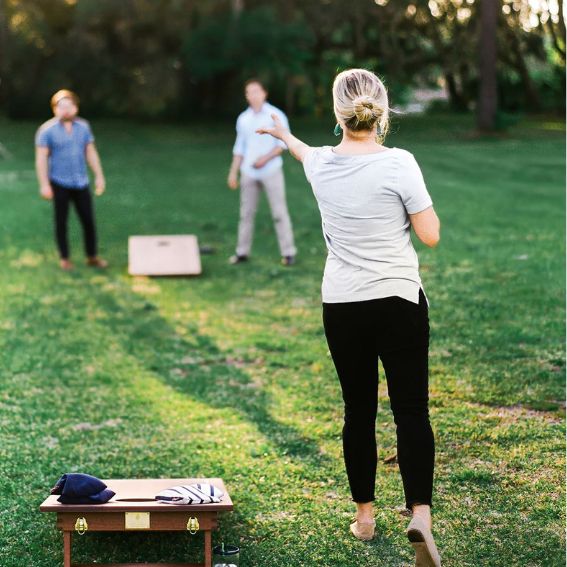 Three people playing cornhole on a grassy lawn in the Wildlight master planned community; one tosses a bean bag while two others stand by the boards, enjoying outdoor fun near new homes in Wildlight, FL.