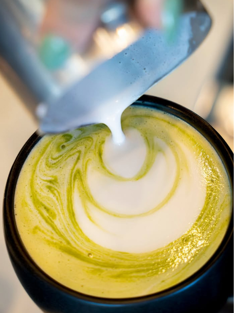 A close-up of milk being poured into a matcha latte, creating swirling patterns on the green and white surface—perfect for cozy mornings in the Wildlight Yulee Florida community.