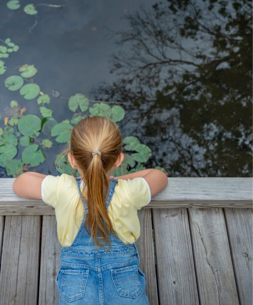 Child staring into pond with lily pads