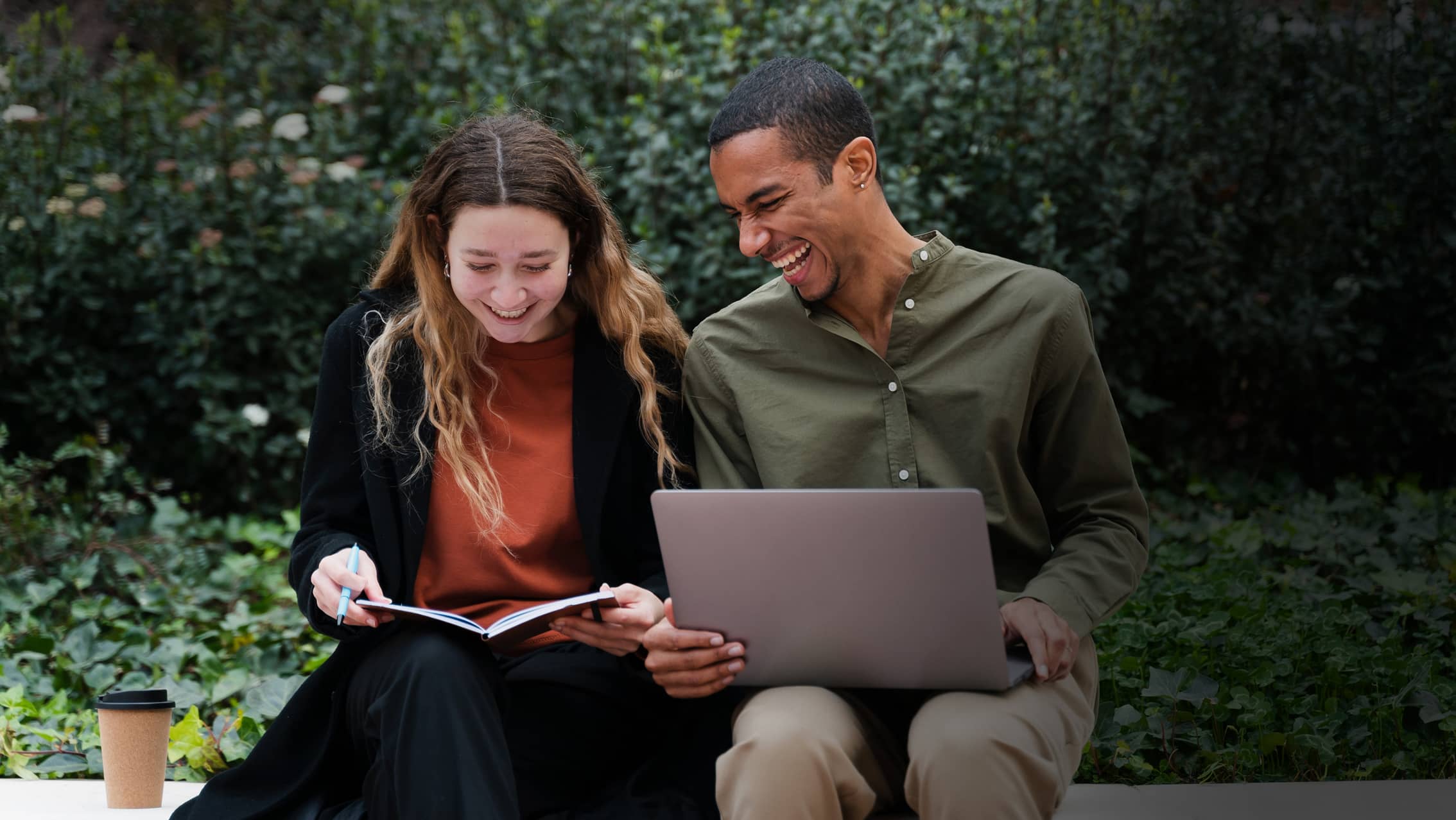 Couple looking at laptop sharing a joke while sitting on a bench.