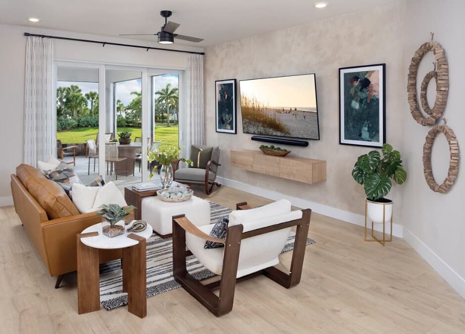 Modern living room with neutral furnishings, wooden accents, wall-mounted TV, large windows, and decor including plants, art, and round mirrors. Outdoor greenery is visible—ideal for those seeking new homes in Wildlight FL.