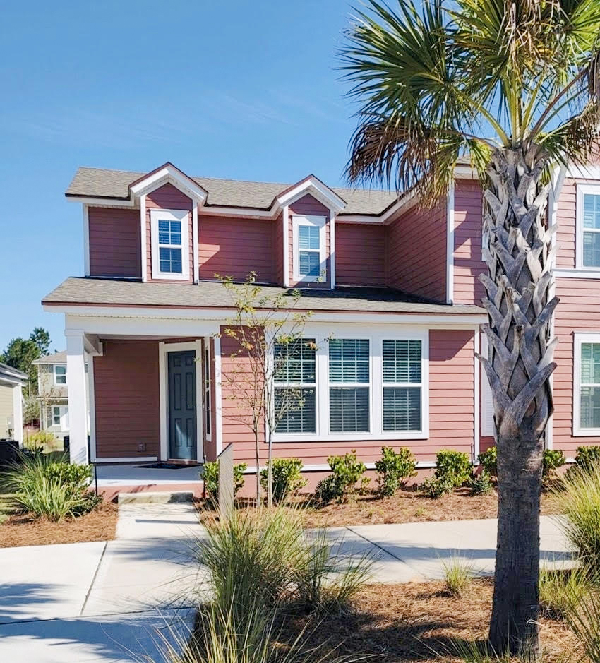 A two-story pink house with white trim, large windows, and a front porch stands behind a palm tree and landscaped yard on a sunny day in the Wildlight master planned community in Wildlight Florida.