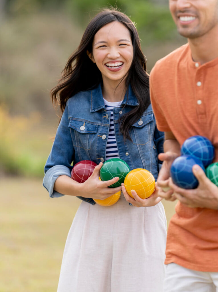 Two people outdoors at the Wildlight Yulee Florida community hold colorful bocce balls, smiling and appearing ready to play.